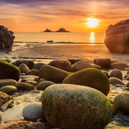 Porth Nanven Cove at sunset with dinosaur boulders in foreground